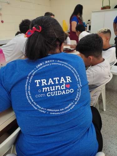 Person in blue shirt with multilingual text sits at a table with children engaged in an activity.