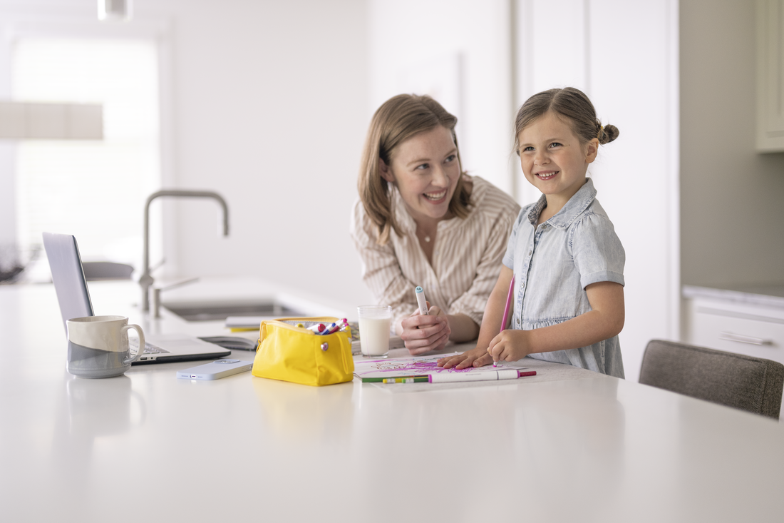 A woman and a young girl are seated at a table and sharing a moment of learning or play.